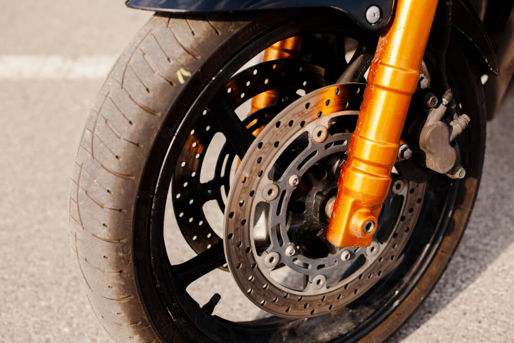 Mâchoire de frein à tambour de moto avec sa garniture usée, à côté d'une colle époxy avec un signe d'interdiction.