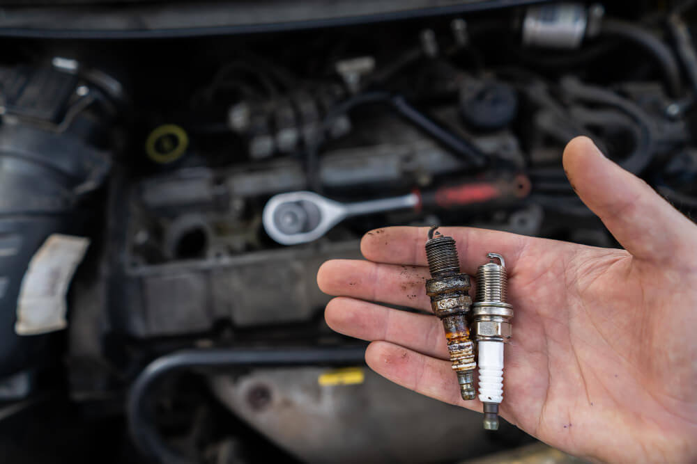Personne tenant une bougie d'allumage contre la culasse d'un moteur pour tester la présence d'une étincelle.