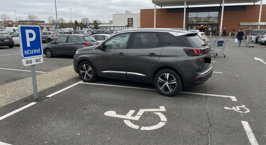 Véhicule garé illégalement sur une place de stationnement réservée aux personnes à mobilité réduite (PMR) sur le parking privé d'un centre commercial