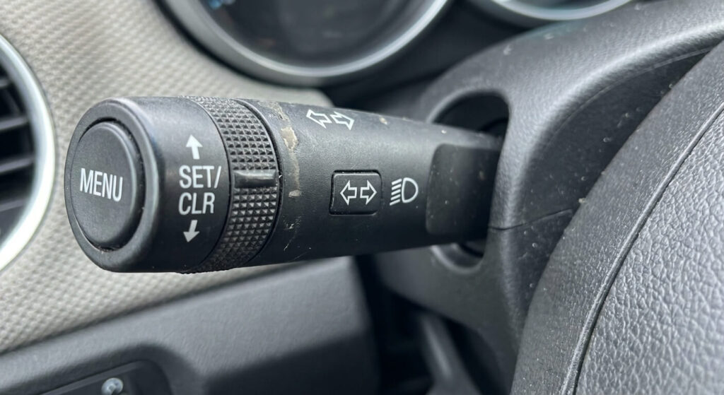 Gros plan sur le commodo de clignotant gauche de la Chevrolet Cruze, équipé du bouton "Menu" et de la molette permettant de naviguer et d'effacer les codes d'entretien