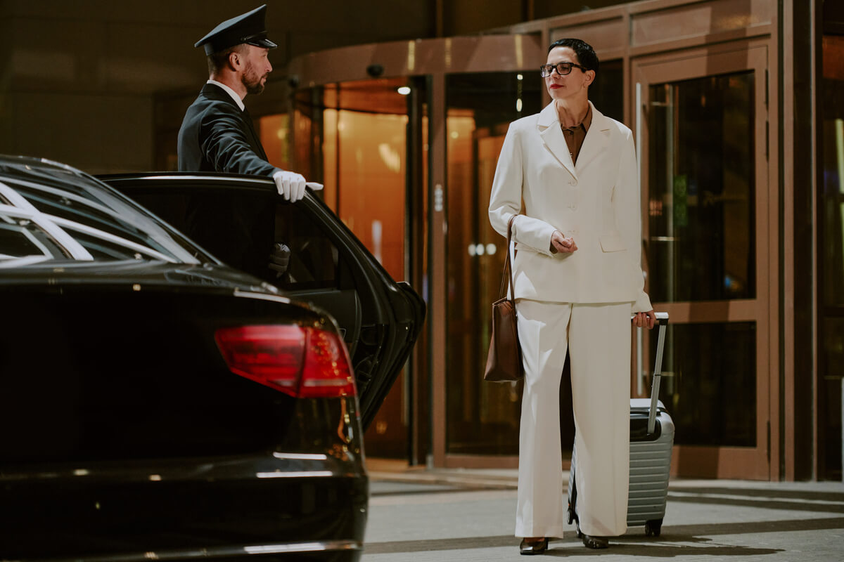 Un chauffeur de limousine en costume accueillant un client VIP à l'aéroport de Genève avec une pancarte.