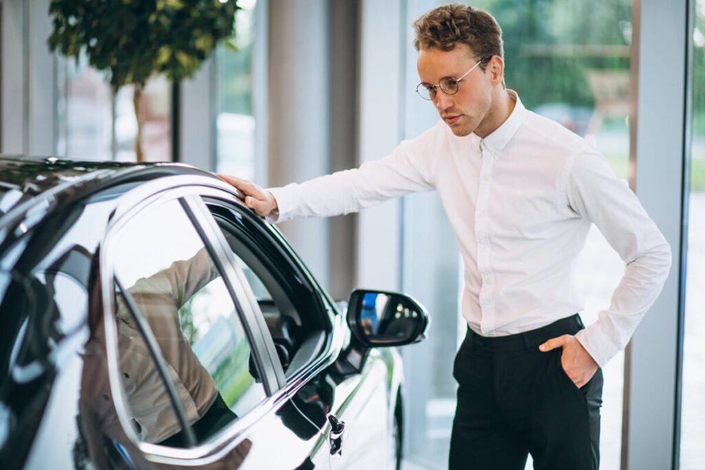 Un acheteur inspectant l'état de la carrosserie d'une voiture d'occasion avant l'achat.