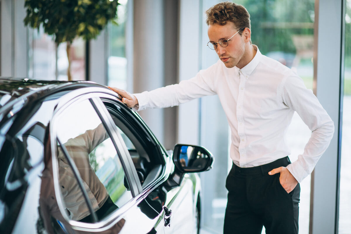 Un acheteur inspectant l'état de la carrosserie d'une voiture d'occasion avant l'achat.