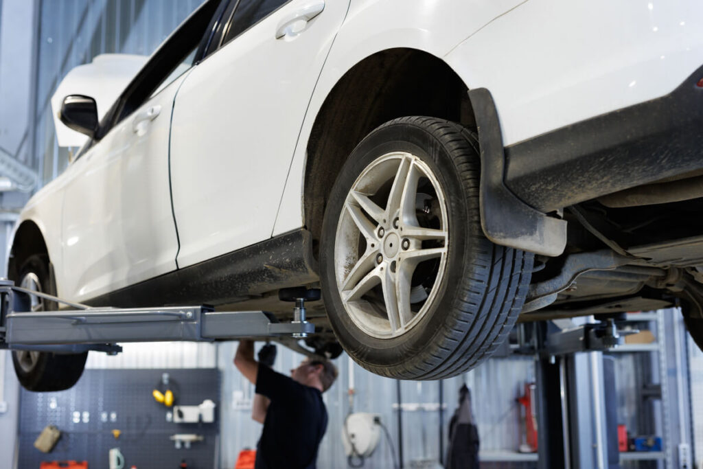 Une voiture sur un pont élévateur dans un garage effectuant un contrôle de parallélisme de la roue avant.