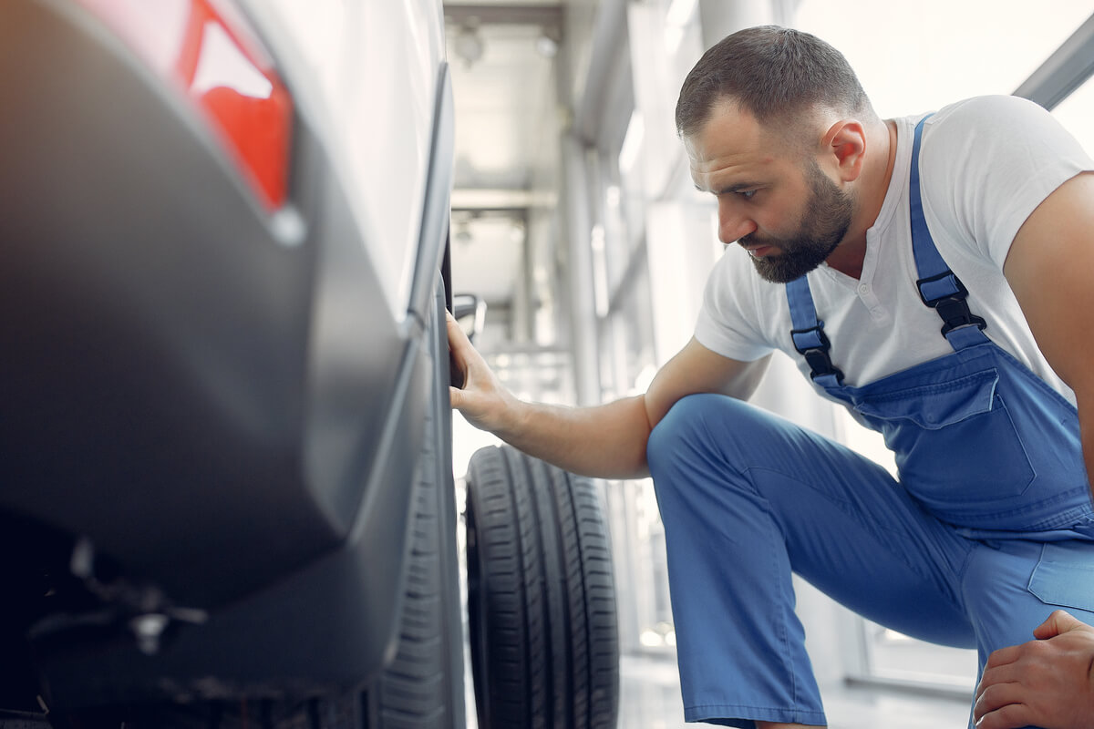 Un technicien automobile mesurant la profondeur des rainures d'un pneu usé avec une jauge de précision.