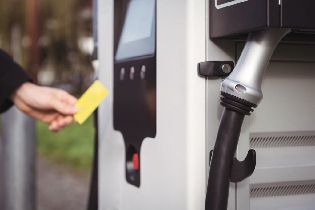 Conducteur passant sa carte de recharge sans contact sur une borne publique pour brancher sa voiture électrique.