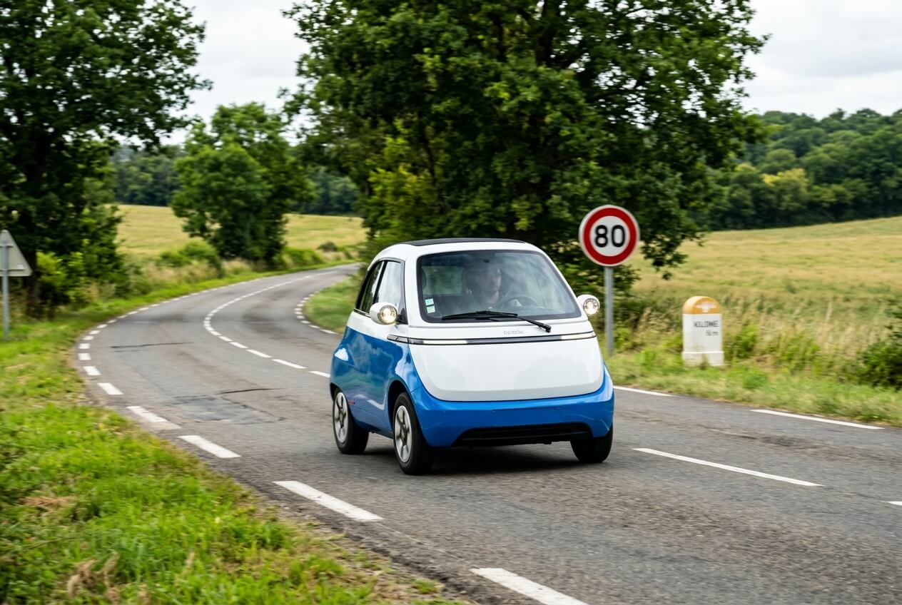 Petite voiture citadine électrique de catégorie L7e roulant sur une route secondaire à 80 km/h.